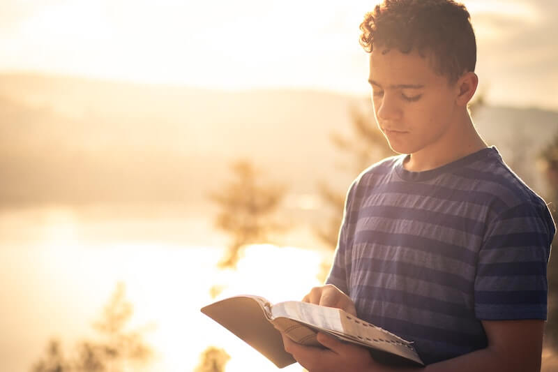 TBI Therapist Blog post of a younger male looking down reading a book at sunset.